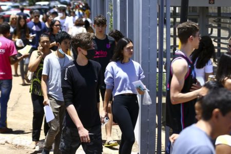 Imagem colorida de estudantes chegando ao colégio para aplicação da prova do Enem 2022