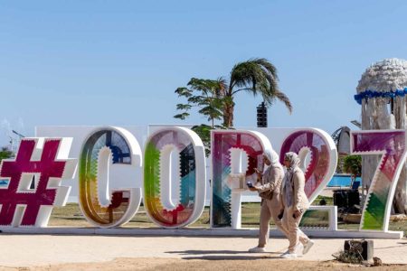 Participantes caminham em frente ao logotipo da COP27 na Zona Verde no quarto dia da COP27 Conferência das Nações Unidas sobre Mudanças Climáticas, realizada pela UNFCCC no Sharm El-Sheikh International Convention Center