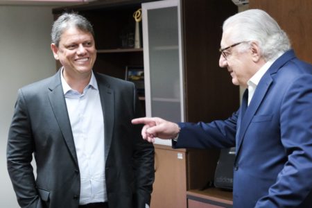 O governador eleito Tarcísio de Freitas e o coordenador da Transição, Guilherme Afif conversam em sala. Ambos estão de pé e sorriem - Metrópoles