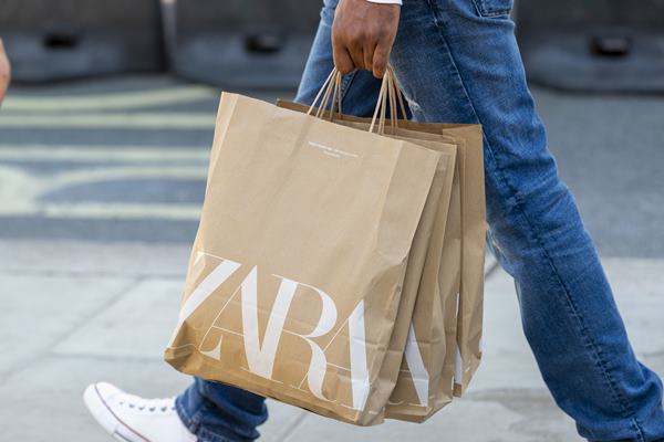 Pessoa branca caminhando na rua segurando três sacolas da Zara - Metrópoles
