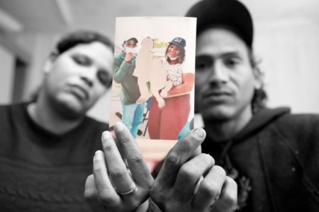 Imagem em preto e branco: mulher e homem seguram fotos com os filhos