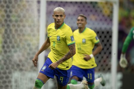 O jogador da seleção brasileira Richarlison comemora gol contra Sérvia na Copa do Mundo do Catar. Ele corre pelo campo, próximo ao gol - Metrópoles