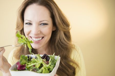 Mulher branca, de cabelos longos e claros está sorrindo e segurando um recipiente com saladas - Metrópoles