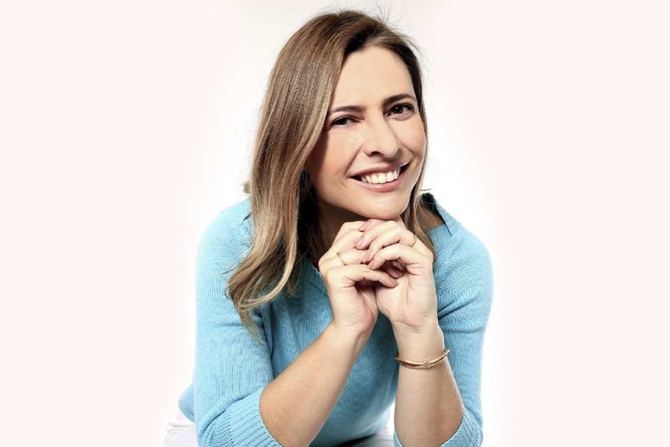 Anna Paula Seifert está sentada com a mão no queixo e sorrindo - Metrópoles