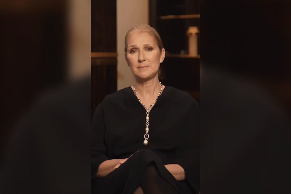 Celine Dion olhando fixamente para a câmera com semblante triste e braços cruzados, síndrome da pessoa rígida (SPR), uma doença rara que debilita o movimento dos membros e causa espasmos inesperados - Metrópoles