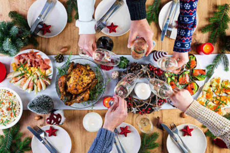 Imagem colorida em que aparece uma mesa e várias pessoas fazendo um brinde de Natal - Metrópoles