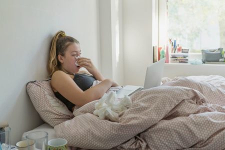 Foto colorida de mulher resfriada na cama assoando o nariz - Metrópoles