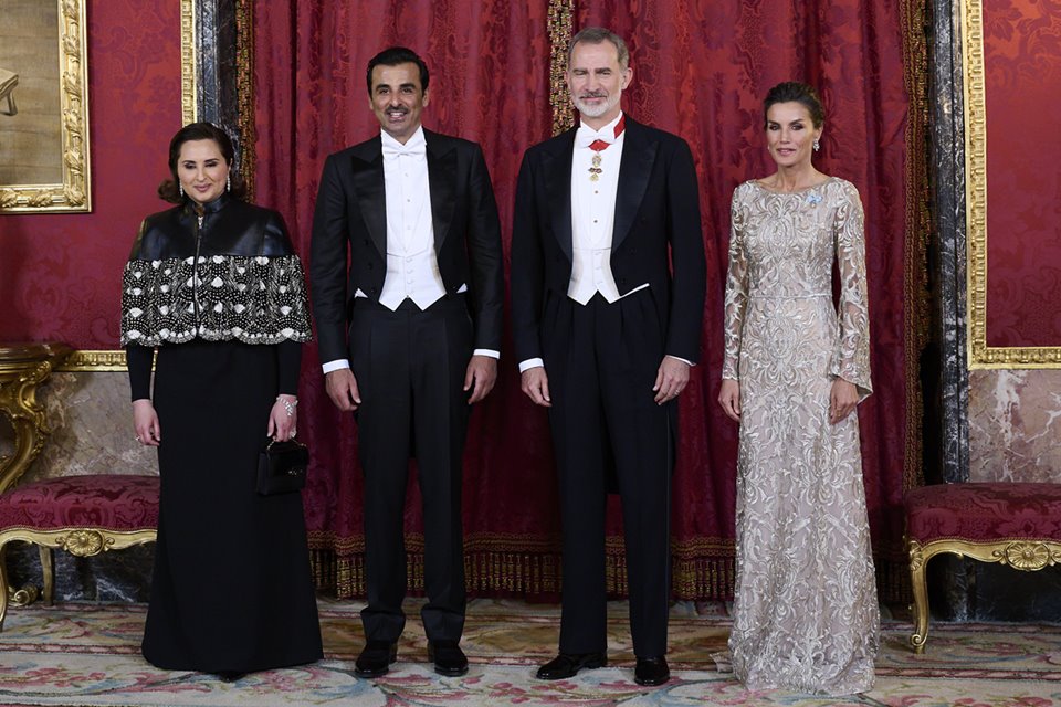 Dois homens e duas mulheres com roupas de gala lado a lado. Eles estão em frente a uma cortina vermelha - Metrópoles