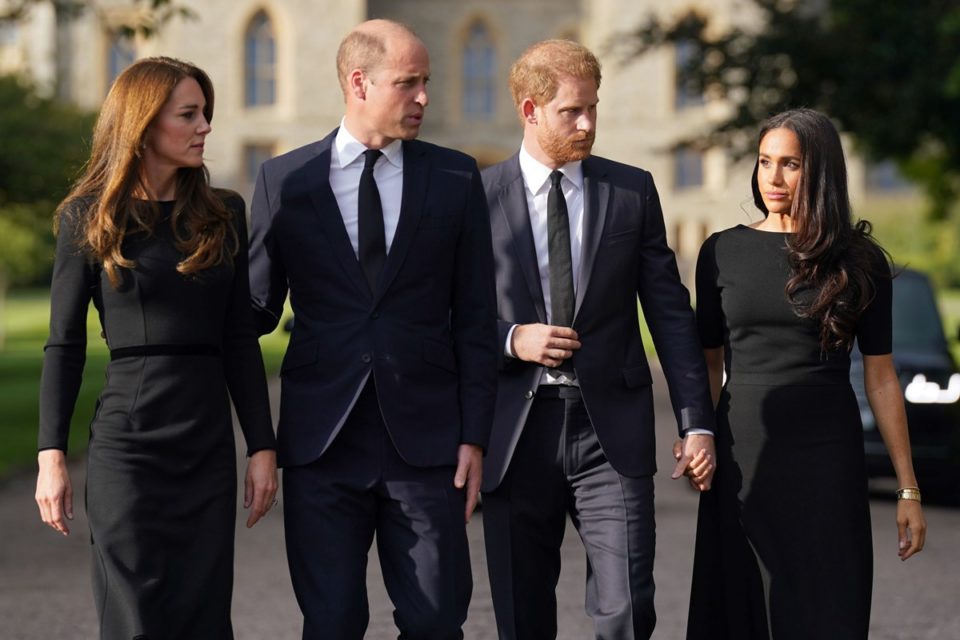 Foto colorida de dois casais lado a lado. Eles são brancos e usam roupas pretas - Metrópoles