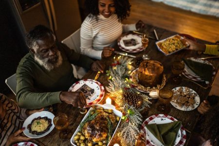 Família à mesa durante a ceia do Natal. Na imagem é possível ver mãe, pai e filha, todos negros e com roupas brancas, pretas e verde. - Metrópoles