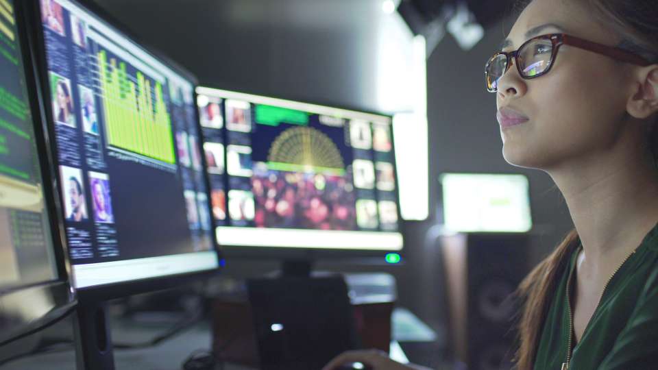 Na foto, há um mulher olhando para dois computadores a frente - Metrópoles