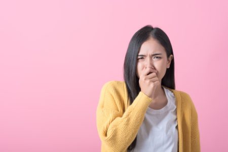 Imagem colorida: mulher de casaco amarelo faz careta com a mão no nariz - Metrópoles