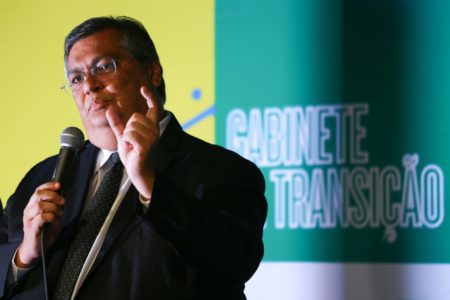 Flávio Dino, indicado para o Ministério da Justiça durante coletiva de imprensa fala ao fundo amarelo e verde - Metrópoles