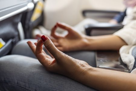 Imagem que foca nas mãos de mulher meditando em avião - Metrópoles