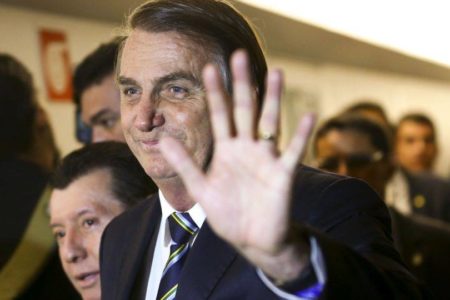 O presidente Bolsonaro em evento, cercado de apoiadores, sorri e cumprimenta-os acenando - Metrópoles