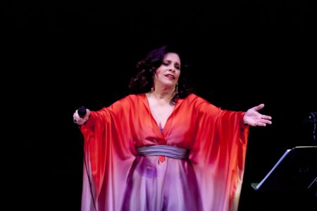 Cantora Gal Costa em show. Na imagem, ela aponta o microfone para a plateia. Usa vestido nas cores vermelho e roxo - Metrópoles