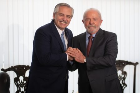 O presidente da Argentina, Alberto Fernández, posa com Lula para foto enquanto apertam as mãos. Ambos sorriem - Metrópoles