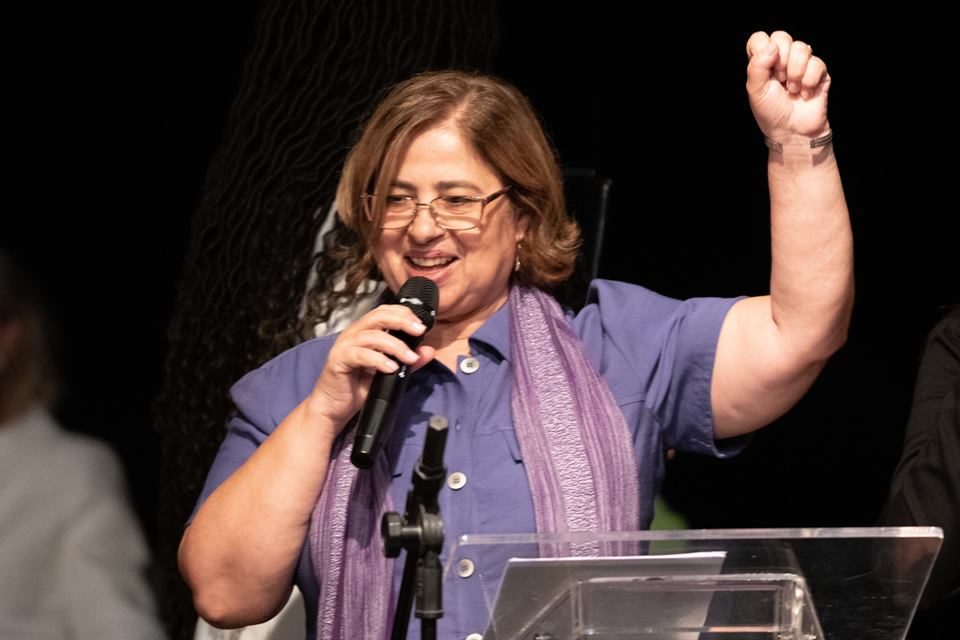 Posse do cargo da nova ministra das Mulheres, Cida Gonçalves, no CCBB. Ela ergue o punho em riste, falando em microfone, e sorri - Metrópoles