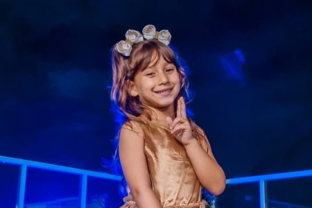 Imagem colorida: menina sentada sorrindo e com tiara na cabeça - Metrópoles