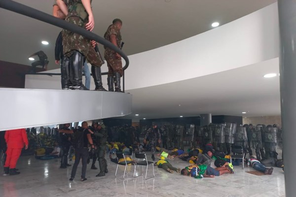 fotografia colorida mostra homens deitados no chão com exército em pé