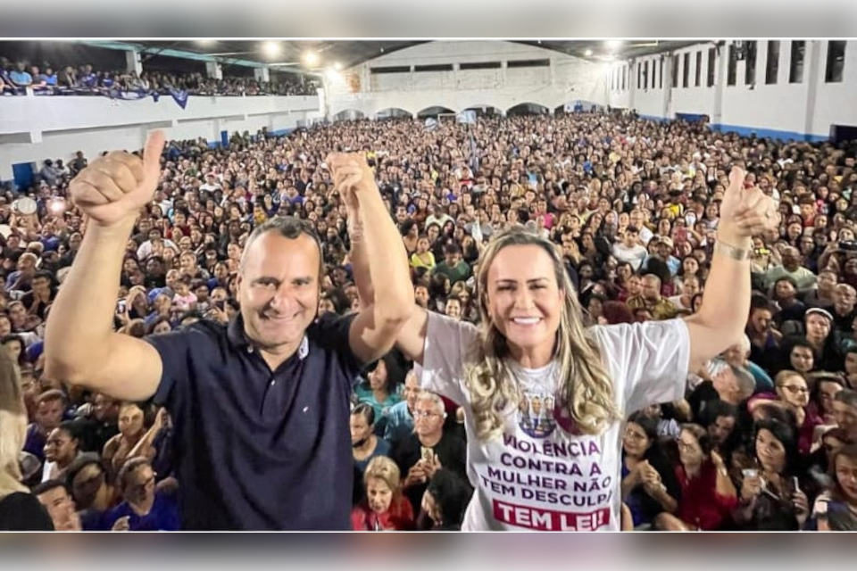 homem e mulher com braços dados erguidos sorriem em frente a multidão