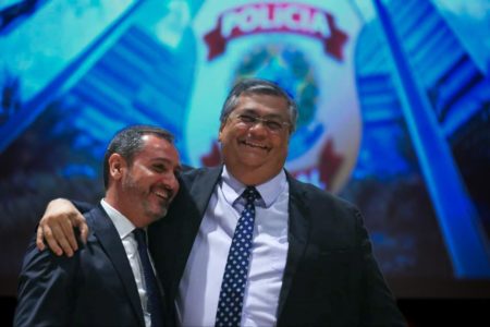 Andrei Rodrigues, novo diretor-geral da PF, abraça o ministro da Justiça e Segurança Pública, Flávio Dino. Eles sorriem diante de painel da Polícia Federal - Metrópoles