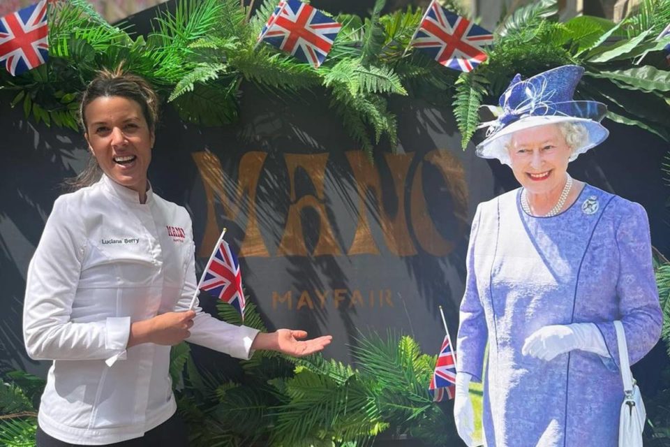 Foto colorida de mulher parda e vestida com dólmã ao lado de boneco da rainha Elizabeth - Metrópoles