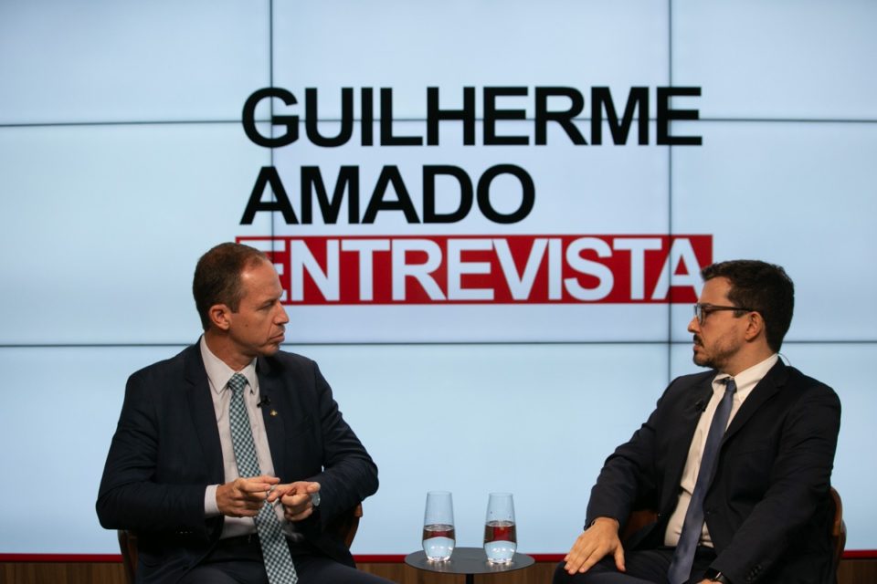 Guilherme Amado entrevista o interventor da segurança pública do DF, Ricado Capelli no Metrópoles. Ambos aparecem sentados lado a lado com um painel atrás - Metrópoles