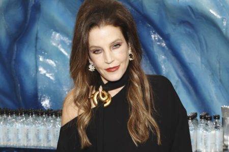 Lisa Marie Presley posa para fotos no Globo de Ouro. Ela utiliza um vestido preto, com detalhes em dourado e brincos pretos - Metrópoles