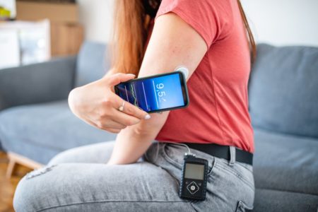 Imagem colorida: mulher monitora diabetes com implante no braço e celular - Metrópoles