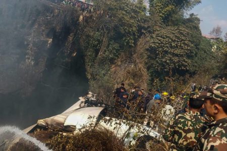 Imagem colorida de vegetação e a turbina branca de um avião após queda no Nepal