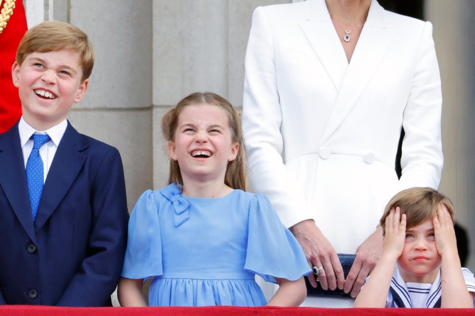 Foto colorida de menino branco, loiro e de terno ao lado de menina branca, loira e com vestido azul ao lado de menino branco, loiro e com as mãos na cabeça - Metrópoles