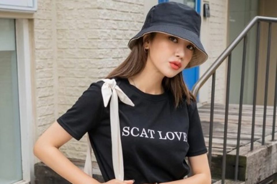 Na imagem, modelo asiática usa chapéu e camiseta preta com a escrita "Scat love", em anúncio da Shein - Metrópoles