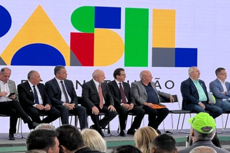 O presidente Lula (ao centro) aparece sentado ao lado do ministro da Previdência, Luiz Marinho em cerimônia com representantes de sindicatos no Palácio do Planalto. Eles aparecem sentados em palco - Metrópoles