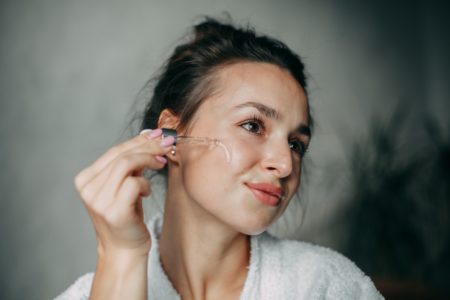 Foto colorida de mulher parda, com cabelo amarrado e passando produto no rosto - Metrópoles