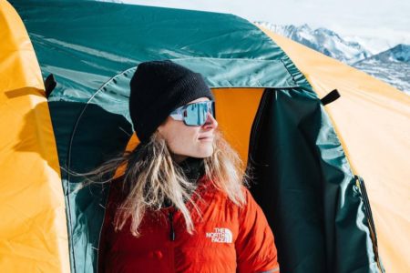 Imagem colorida: mulher em frente à barraca de acampamento em montanha - Metrópoles