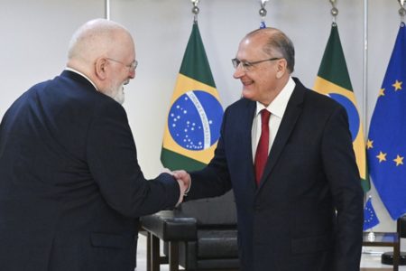Frans Timmermans, representante da União Europeia, e Geraldo Alckmin, presidente em exercício do Brasil, apertam as mãos após encontro. Eles sorriem e se vê a fundo as bandeiras respectivas - Metrópoles