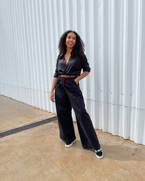 Mulher negra de cabelo cacheado usa calça jeans preta, camiseta preta e sandália - Metrópoles