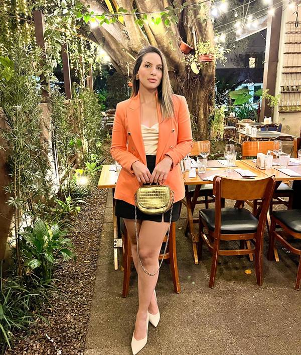 Mulher branca usa blazer laranja, camisa branca, saia preta e sapato - Metrópoles