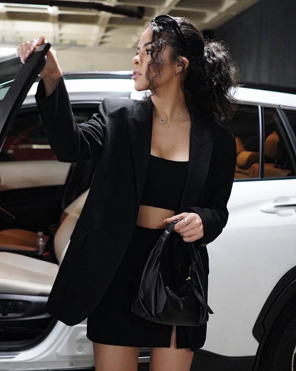 Mulher negra de cabelo cacheado usa top preto e blazer preto - Metrópoles