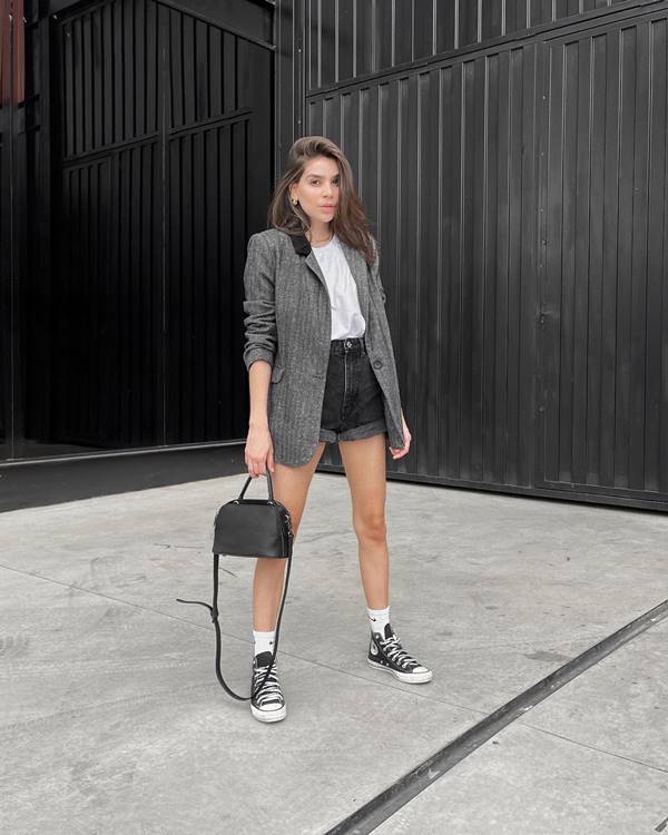 Mulher branca usa blazer cinza, blusa branca, shorts e tênis converse - Metrópoles