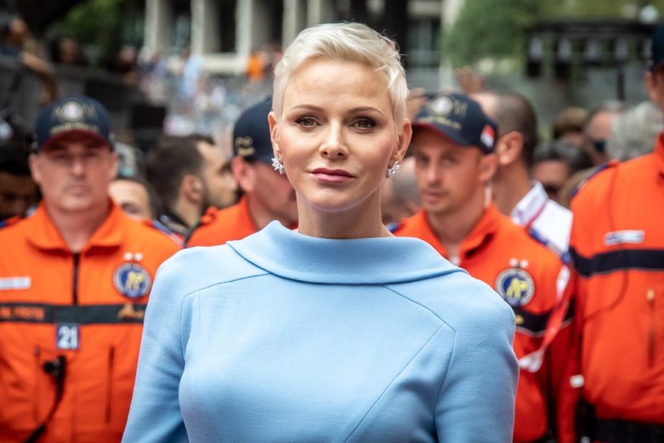 Foto colorida de mulher branca, com cabelo platinado e roupa azul candy com pessoas atrás usando roupa na cor laranja - Metrópoles