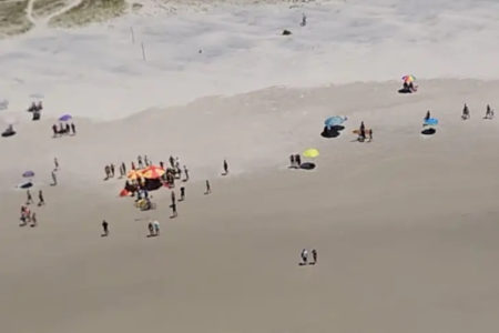 imagem aérea de praia com pessoas e embarcação virada