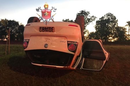 Carro branco de cabeça para baixo em gramado e com porta aberta