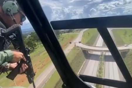 Fotografia colorida mostra policial armado em helicóptero