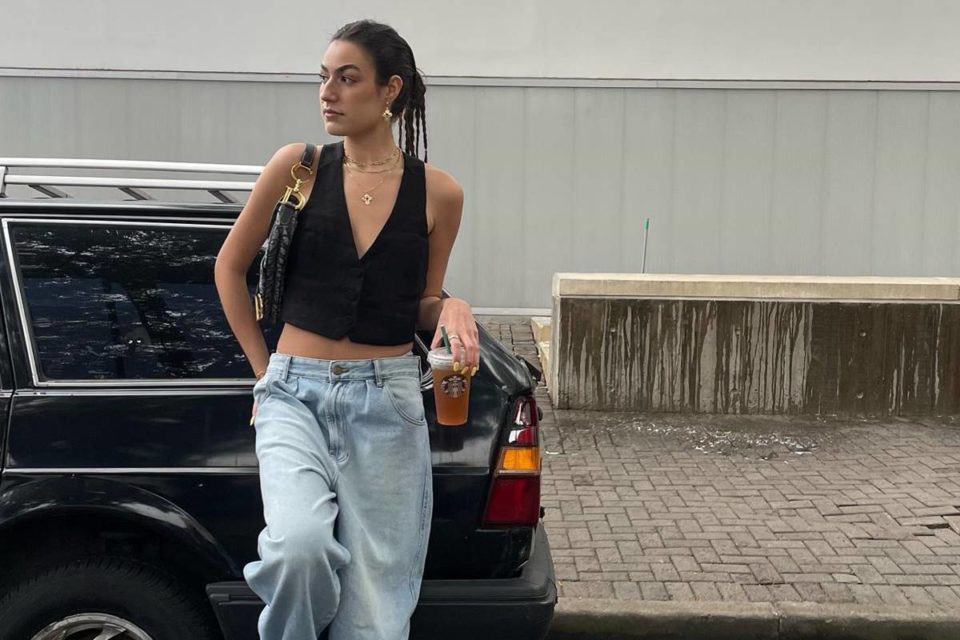 Influencer posa encostada em carro com colete preto e calça jeans de cintura baixa - Metrópoles