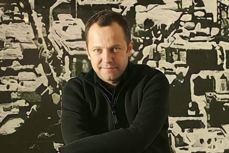 Foto do artista Vik Muniz. Ele usa casaco preto e está de braços cruzados - Metrópoles