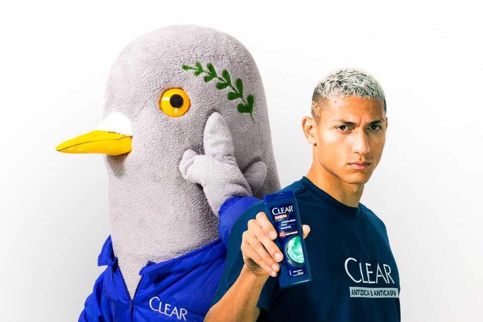 Na foto está o jogador Richarlison segurando um shampoo da Clear e, ao lado dele, um pombo de pelúcia - Metrópoles