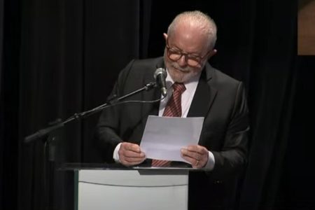 O presidente Lula discursa em púlpito, lendo folha de papel, sobre países devedores do BNDES durante cerimônia - Metrópoles