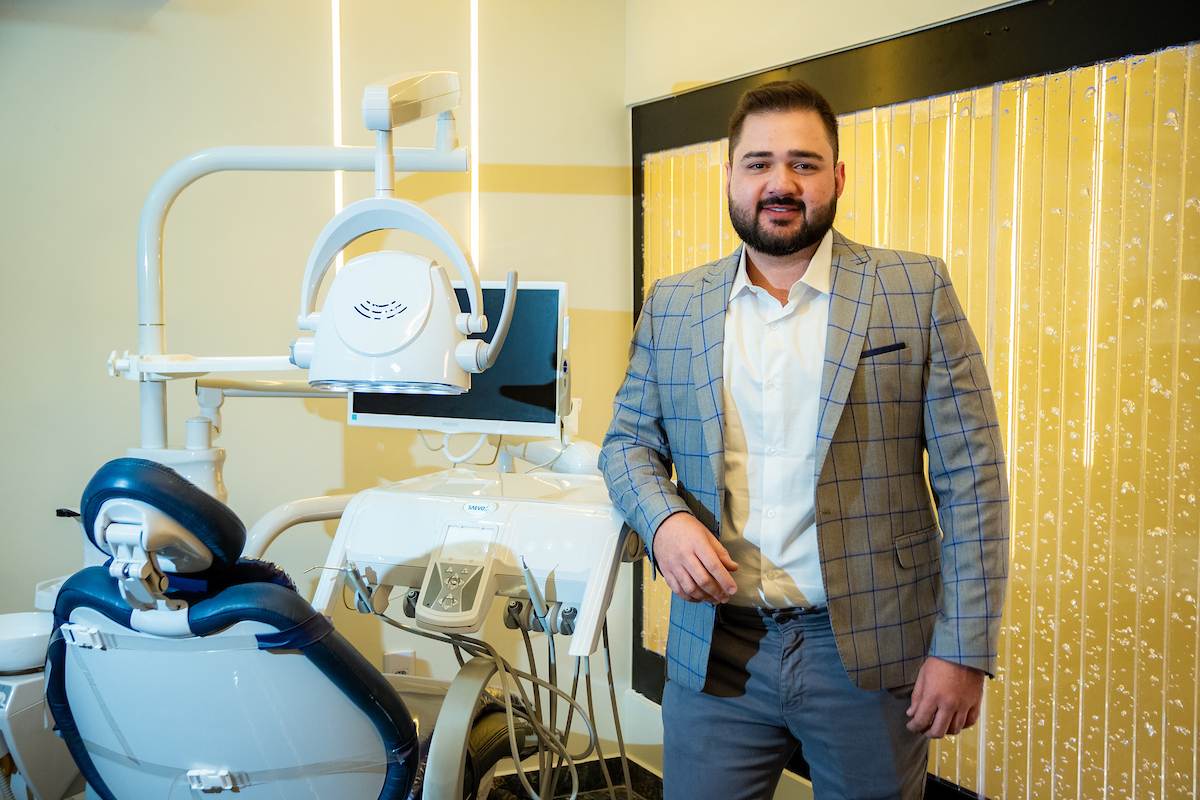 Foto colorida de um homem ao lado de uma cadeira de dentista